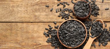 Bowls and spoon with sunflower seeds on wooden background with space for text