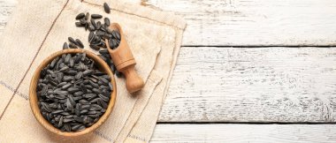Bowl and scoop with sunflower seeds on wooden background with space for text