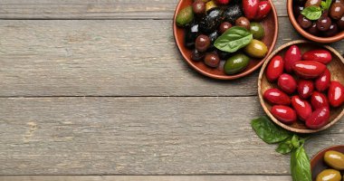 Plates with different types of delicious olives on wooden background with space for text