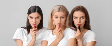 Beautiful young women applying lipstick against light background