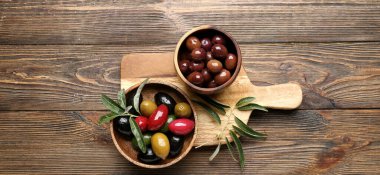 Bowls with different types of tasty olives on wooden background