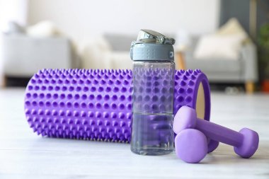 Foam roller with bottle of water and dumbbells in living room