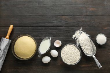 Raw dough with ingredients and utensils on dark wooden background