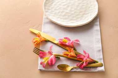 Table setting with plate, cutlery and alstroemeria flowers on beige background