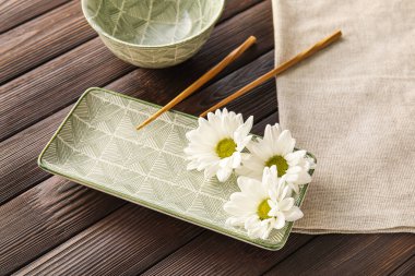 Table setting with chopsticks and chamomile flowers on wooden background