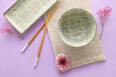 Stylish table setting with chopsticks and flowers on color background