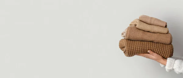 Female hands with stack of warm knitted sweaters on light background with space for text