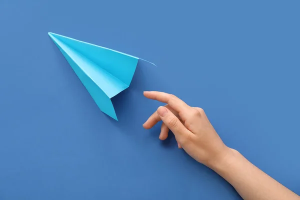 Woman with blue paper plane on color background