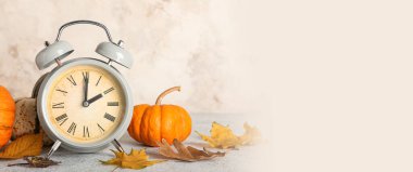 Alarm clock and autumn leaves with pumpkins on light background. Banner for design