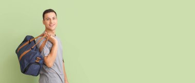 Sporty young man with bag on green background with space for text