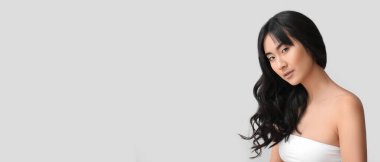 Young Asian woman with beautiful long wavy hair on light background with space for text
