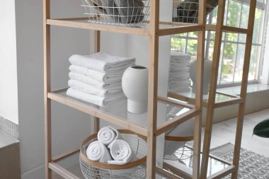Wooden shelving unit with clean towels and vase near light wall