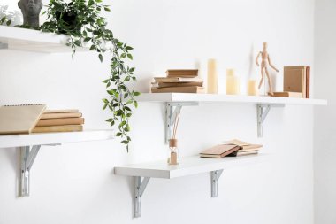 Shelves with books, decor and candles hanging on light wall