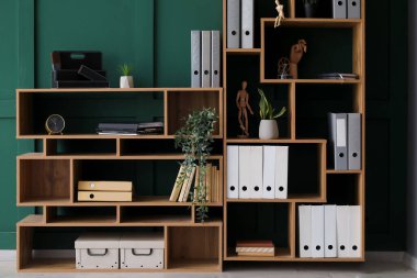 Wooden shelving unit with folders and decor near green wall