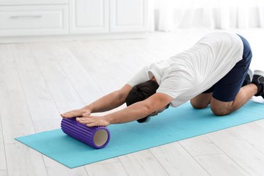 Young man training with foam roller in kitchen
