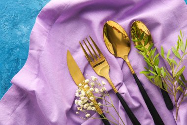 Stylish cutlery and floral decor on napkin against blue background