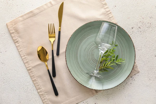 Elegant table setting with plate, cutlery, glass and plant branch on light background