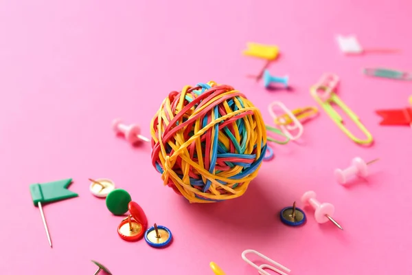 Ball made of colorful rubber bands, paper clips and pins on pink background, closeup