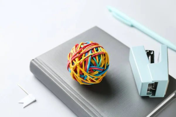 Colorful rubber band ball, stapler and notebook on white background, closeup