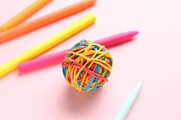 Colorful rubber band ball and different pens on pink background, closeup