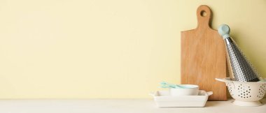 Set of kitchen utensils on table against yellow background with space for text