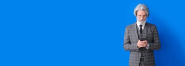 Portrait of senior businessman using mobile phone on blue background with space for text