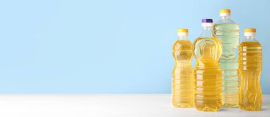 Bottles of sunflower oil on table against light blue background with space for text