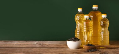 Bottles of sunflower oil on table against dark green background with space for text