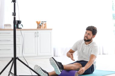 Young man with foam roller recording video in kitchen