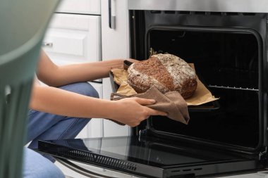 Woman taking out baking tray with fresh bread from oven in kitchen, closeup