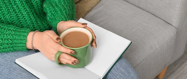 Woman with cup of hot coffee and book at home, closeup