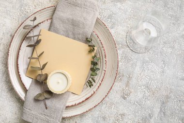 Table setting with blank card, eucalyptus branches and candle on grey background