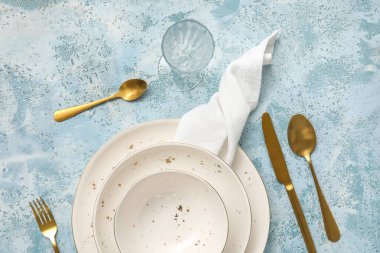 Simple table setting with plates, cutlery and glass on blue background