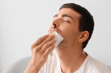 Young man wiping nosebleed with tissue at home, closeup
