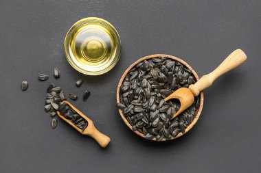 Bowls with sunflower seeds, oil and scoop on black background
