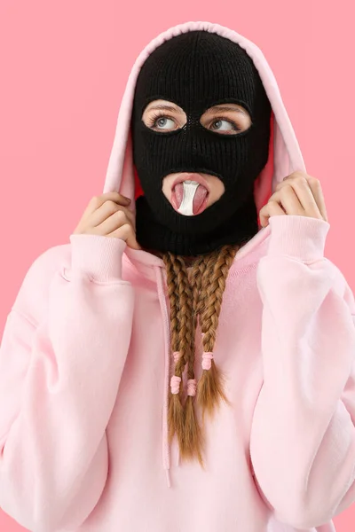 Young woman in balaclava with gum against pink background