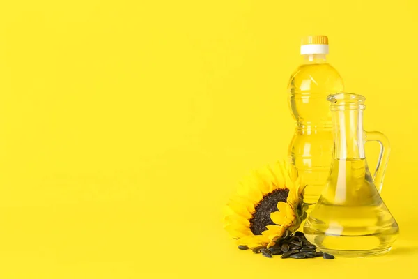 Beautiful sunflower with black seeds, jug and bottle of oil on yellow background