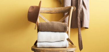 Wooden chair with stack of sweaters and hat near yellow wall in room