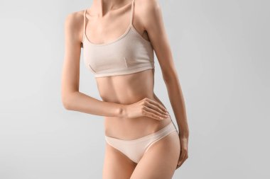 Slim young woman in underwear on light background