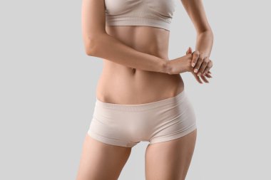 Slim young woman in underwear on light background