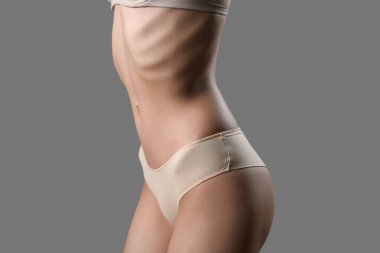 Gri arka planda iç çamaşırlı zayıf genç bir kadın.