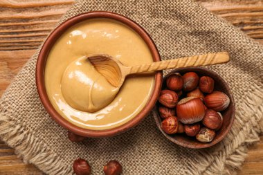 Bowls of tasty hazelnut butter and nuts on wooden background, closeup