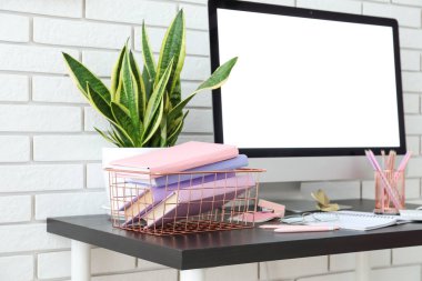 Basket with books, computer and houseplant on table near white brick wall