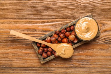Board with tasty hazelnut butter and nuts on wooden background
