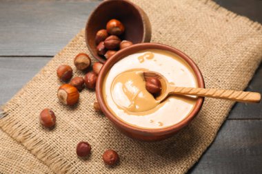 Bowls with tasty hazelnut butter and nuts on dark wooden background