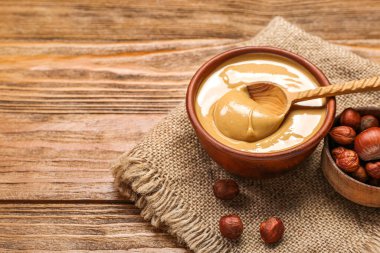Bowls of tasty hazelnut butter and nuts on wooden background