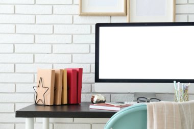 Holder with books, computer and pen cup on table near white brick wall