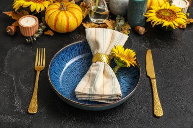 Dinnerware with sunflower in plate and autumn decor on dark table