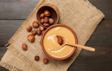 Bowls with tasty hazelnut butter and nuts on dark wooden background