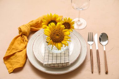 Stylish dinnerware and sunflowers in plate on beige table